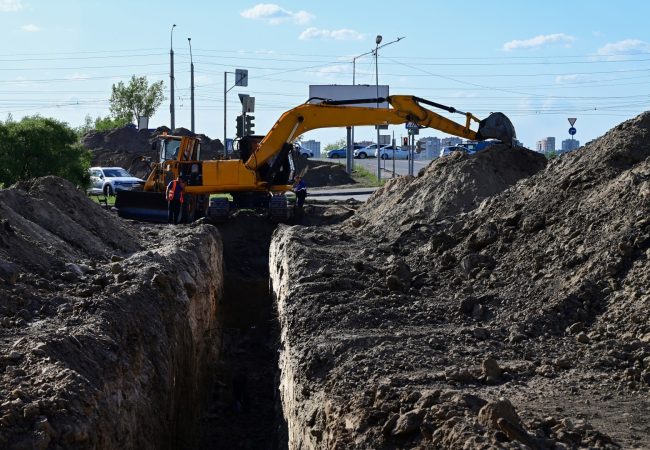 Excavator during earthmoving at open pit on blue sky background. Construction machinery and earth-moving heavy equipment for excavation, loading, lifting and hauling of cargo on job sites